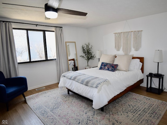 bedroom featuring ceiling fan, visible vents, baseboards, and wood finished floors