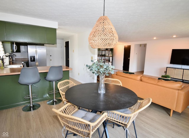 dining space with recessed lighting, light wood-style flooring, a textured ceiling, and baseboards