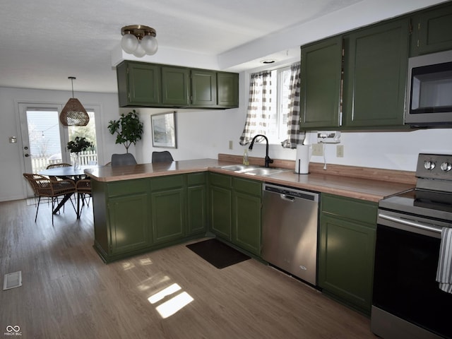 kitchen with a sink, wood finished floors, a peninsula, appliances with stainless steel finishes, and green cabinetry