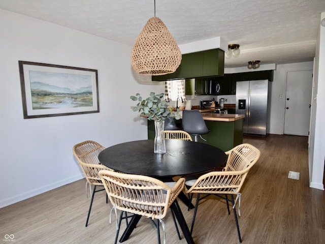 dining area featuring light wood-style floors, baseboards, and a textured ceiling