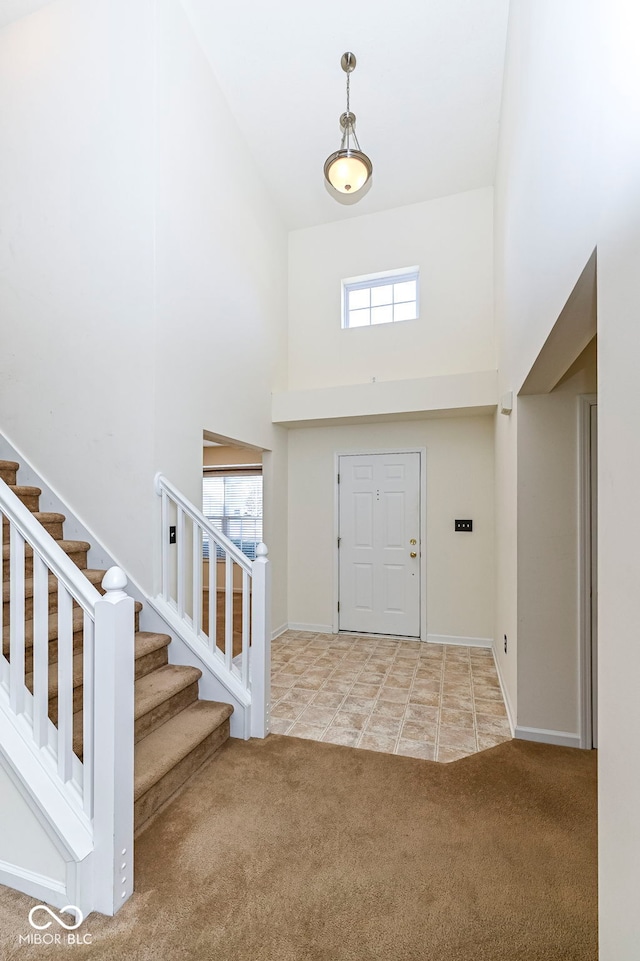 tiled foyer with stairs, a high ceiling, baseboards, and carpet floors