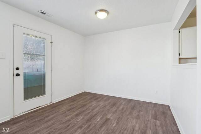 spare room featuring visible vents, dark wood-type flooring, and baseboards