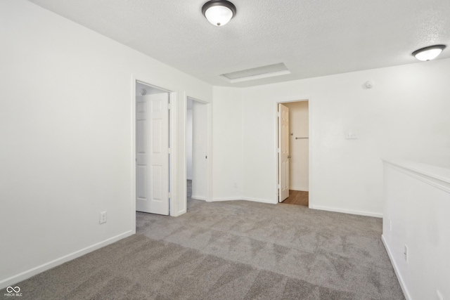carpeted empty room with a textured ceiling, attic access, and baseboards