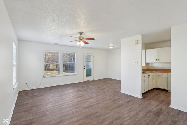 unfurnished living room featuring a ceiling fan, dark wood-style floors, baseboards, and a textured ceiling