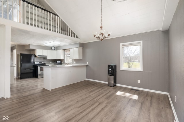 kitchen with wood finished floors, a peninsula, stainless steel electric stove, freestanding refrigerator, and a notable chandelier