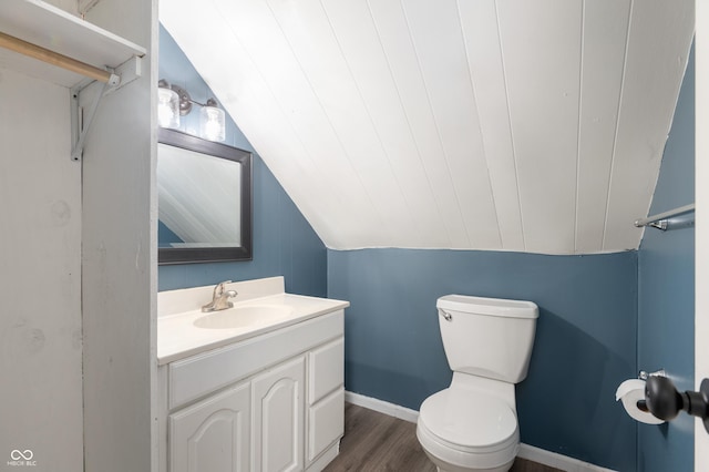half bath featuring toilet, wood finished floors, baseboards, vanity, and vaulted ceiling