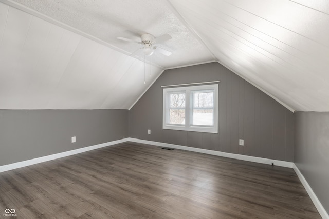additional living space with a ceiling fan, visible vents, baseboards, dark wood-style flooring, and vaulted ceiling