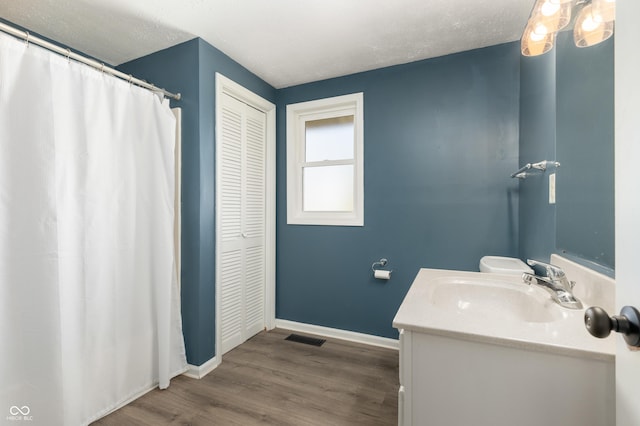 bathroom featuring vanity, wood finished floors, baseboards, visible vents, and a closet