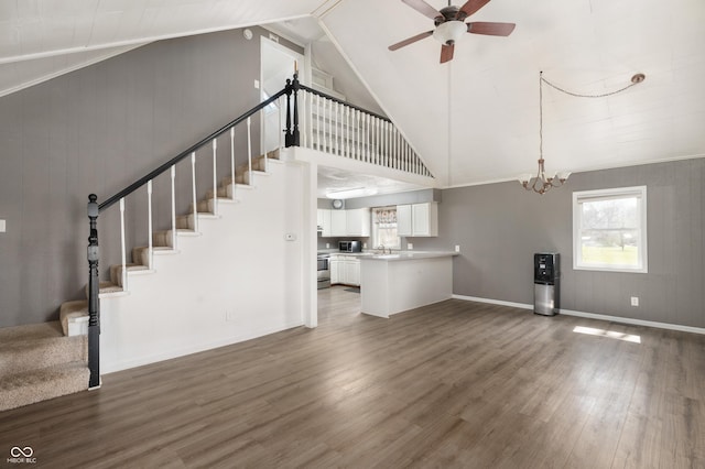 unfurnished living room featuring ceiling fan with notable chandelier, stairs, wood finished floors, and baseboards