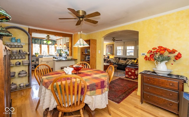 dining area featuring arched walkways, light wood-style floors, a ceiling fan, and crown molding