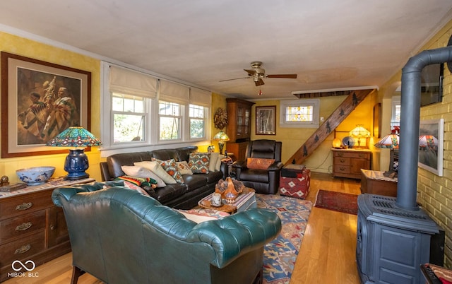 living area with a wood stove, ornamental molding, wood finished floors, and ceiling fan