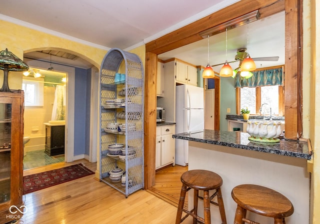 kitchen featuring light wood-style flooring, freestanding refrigerator, ornamental molding, hanging light fixtures, and stainless steel microwave