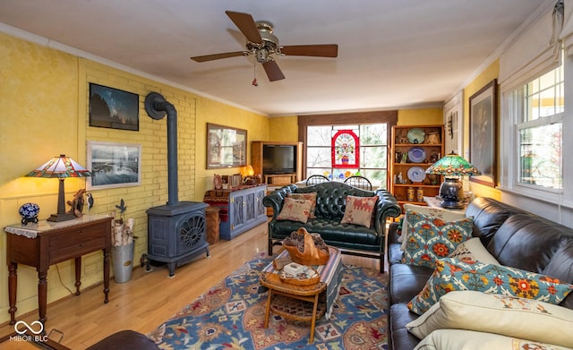 living room with a wood stove, wood finished floors, ornamental molding, and a ceiling fan