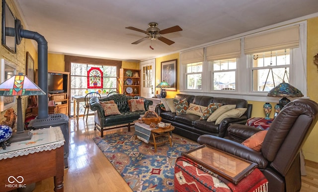 living area featuring wood finished floors, a wood stove, and a ceiling fan