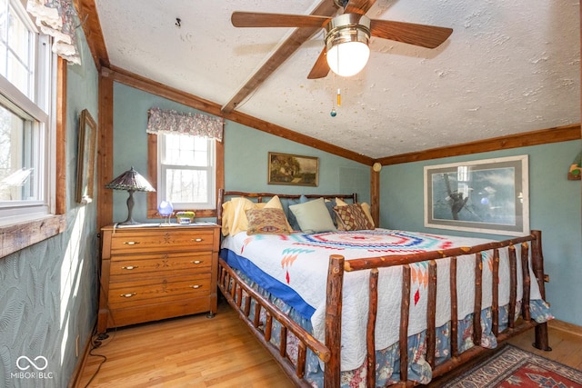 bedroom with a textured ceiling, ceiling fan, vaulted ceiling with beams, and light wood finished floors