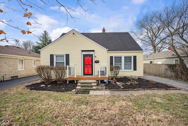 bungalow-style house with a shingled roof, fence, and a chimney