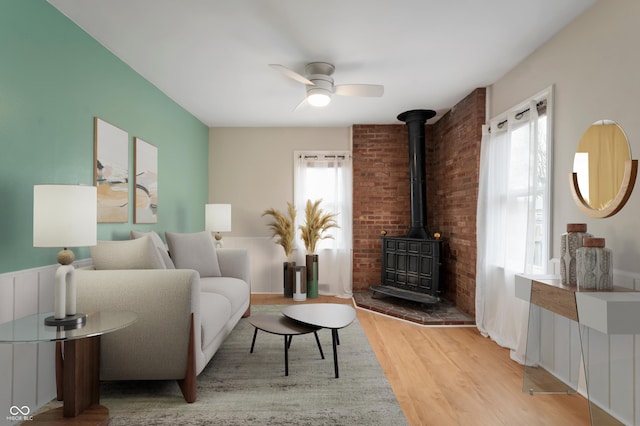 living room featuring plenty of natural light, a wood stove, a ceiling fan, and wood finished floors