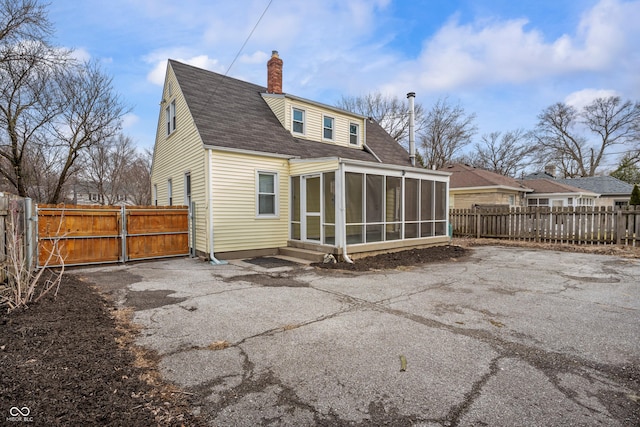 rear view of property with a gate, fence, roof with shingles, a sunroom, and a chimney