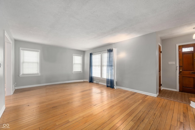 interior space with visible vents, baseboards, light wood-type flooring, and a textured ceiling