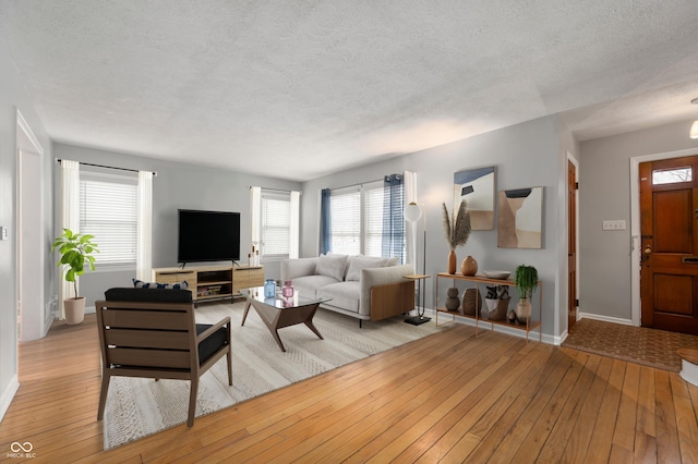 living room with a textured ceiling, light wood-type flooring, and baseboards