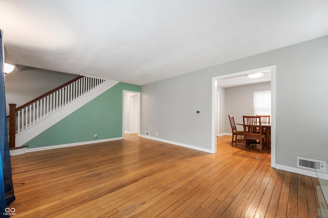 unfurnished living room with stairway, baseboards, visible vents, and hardwood / wood-style floors