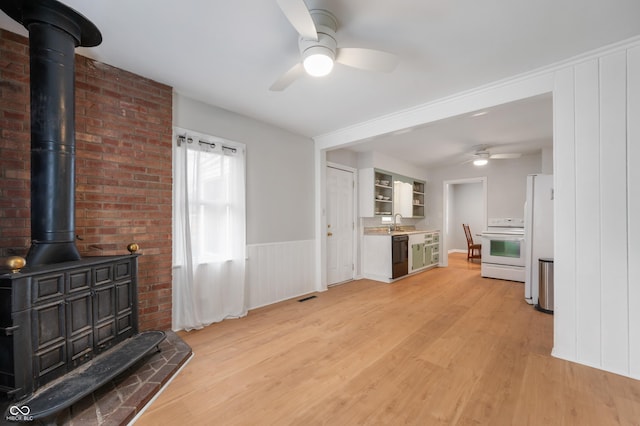 living room with light wood-type flooring, a ceiling fan, visible vents, and a wood stove