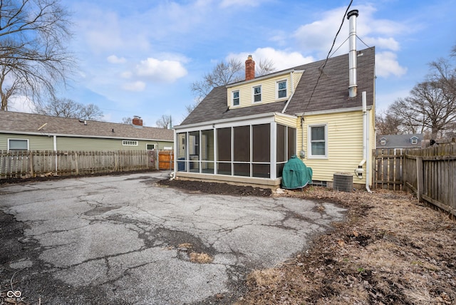 rear view of house featuring cooling unit, roof with shingles, a fenced backyard, a sunroom, and a chimney