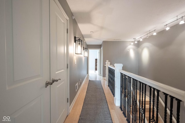 hallway with light wood-type flooring, baseboards, an upstairs landing, and track lighting