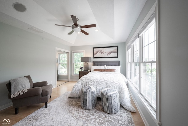 bedroom featuring baseboards, visible vents, light wood-style flooring, ceiling fan, and a raised ceiling