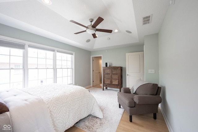 bedroom with light wood-type flooring, visible vents, recessed lighting, baseboards, and a raised ceiling