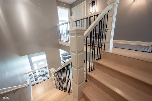 staircase featuring a wealth of natural light, baseboards, wood finished floors, and ornate columns