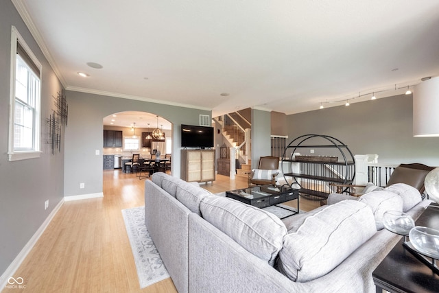 living room featuring stairway, baseboards, light wood finished floors, arched walkways, and crown molding