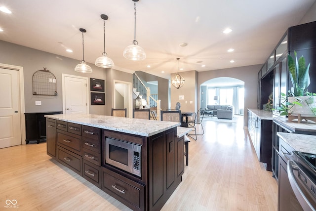 kitchen featuring recessed lighting, stainless steel microwave, arched walkways, and light wood finished floors