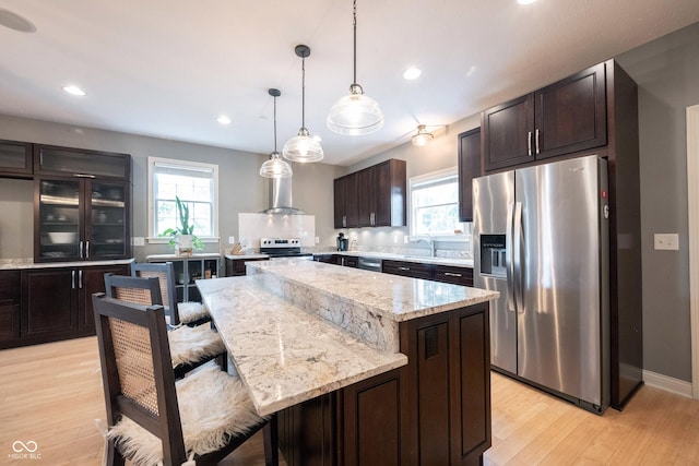 kitchen featuring stainless steel appliances, plenty of natural light, dark brown cabinets, and wall chimney range hood