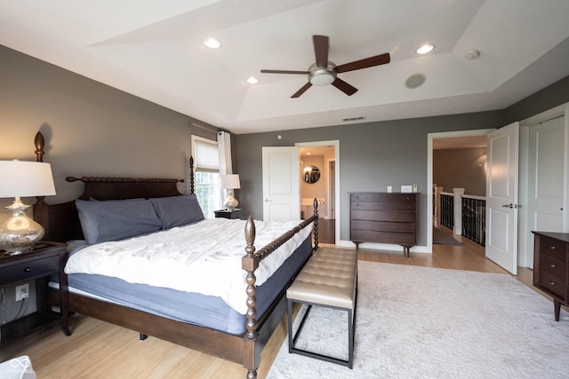 bedroom with a tray ceiling, recessed lighting, visible vents, and light wood-type flooring