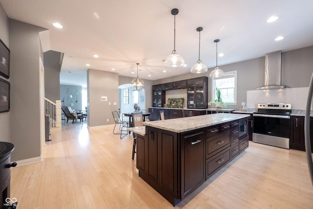 kitchen with wall chimney exhaust hood, light wood-style floors, appliances with stainless steel finishes, and a kitchen island