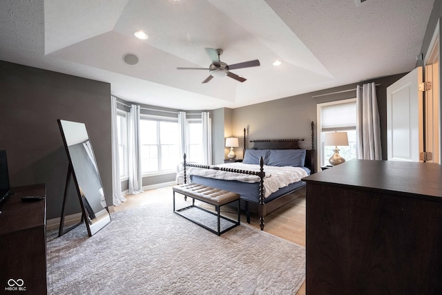 bedroom with baseboards, a tray ceiling, recessed lighting, a textured ceiling, and light wood-type flooring