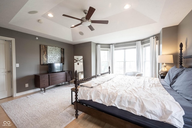 bedroom featuring a tray ceiling, baseboards, and wood finished floors