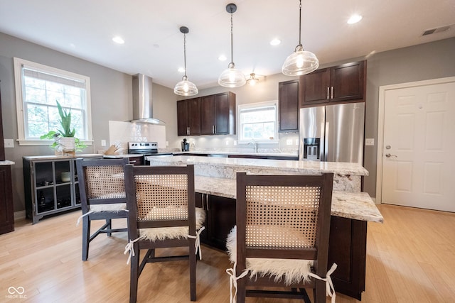 kitchen with visible vents, a center island, stainless steel appliances, wall chimney exhaust hood, and dark brown cabinets