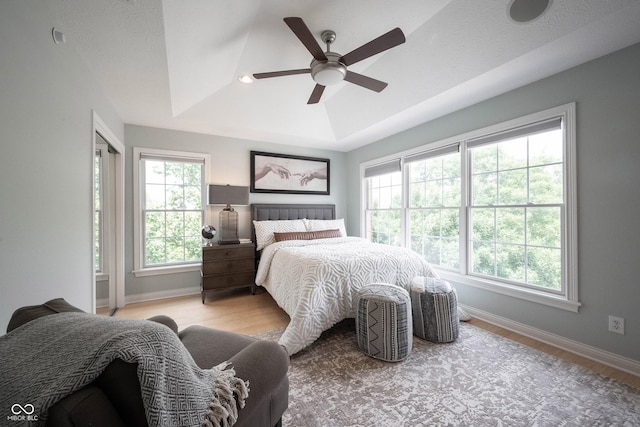 bedroom with a ceiling fan, a raised ceiling, baseboards, and light wood-type flooring