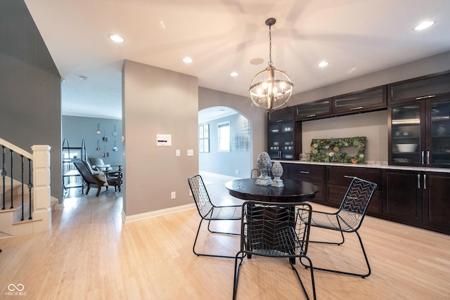 dining area featuring light wood-type flooring, arched walkways, baseboards, a chandelier, and stairs