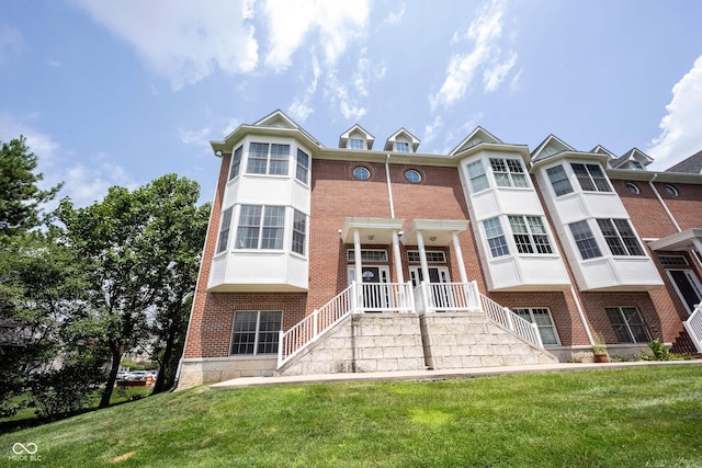 exterior space with brick siding, stairway, and a front yard