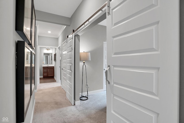 hallway featuring a barn door, light colored carpet, and baseboards