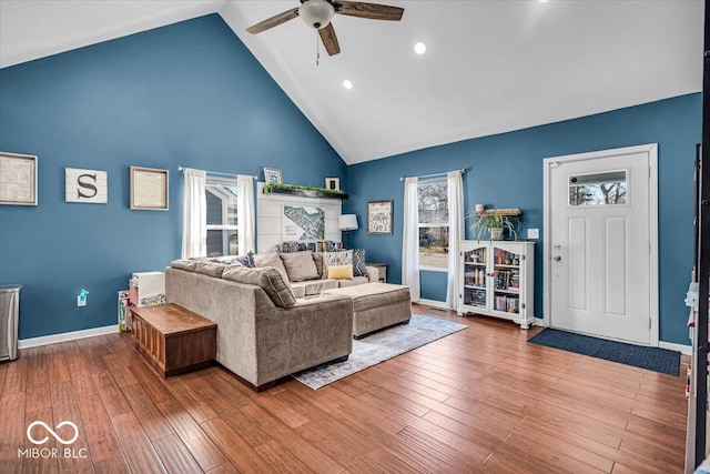 living room featuring baseboards, wood-type flooring, high vaulted ceiling, and ceiling fan