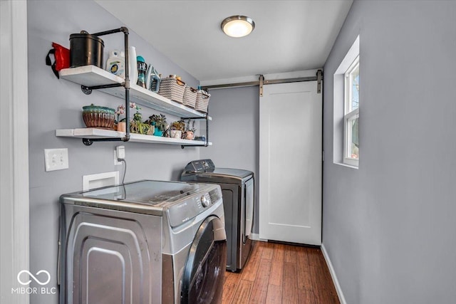 washroom with baseboards, a barn door, laundry area, wood finished floors, and separate washer and dryer