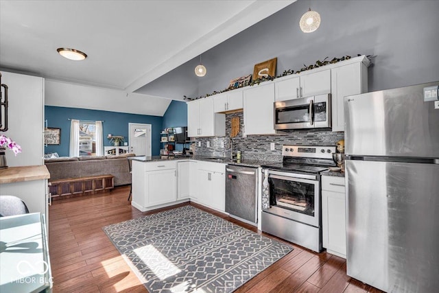 kitchen featuring vaulted ceiling, appliances with stainless steel finishes, a peninsula, white cabinetry, and a sink