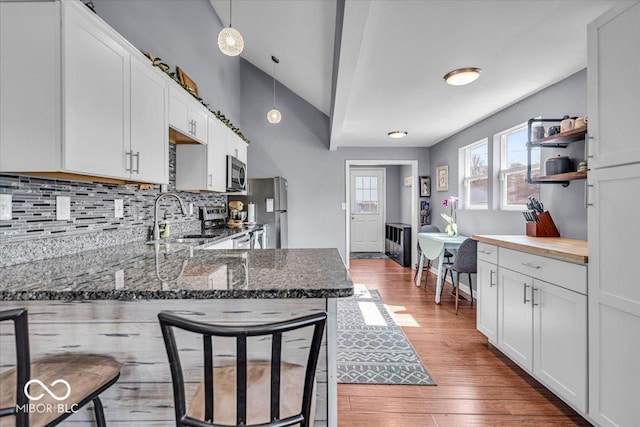 kitchen featuring a breakfast bar, a sink, wood finished floors, white cabinetry, and appliances with stainless steel finishes