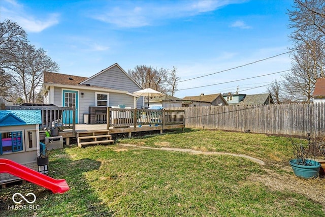 rear view of house with a deck, a playground, a lawn, and fence