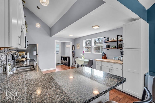 kitchen featuring stainless steel microwave, dark stone countertops, wood finished floors, white cabinetry, and a sink