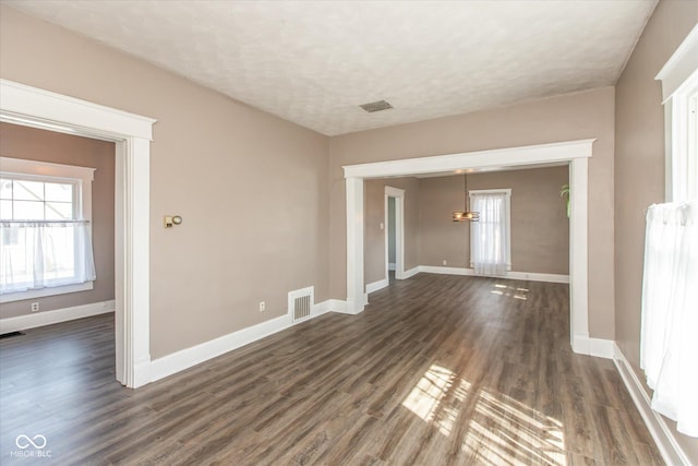 empty room featuring baseboards, visible vents, and dark wood-style flooring